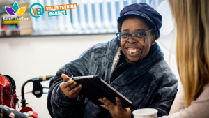 Dark skinned female presenting person smiling at the camera whilst holding an ipad